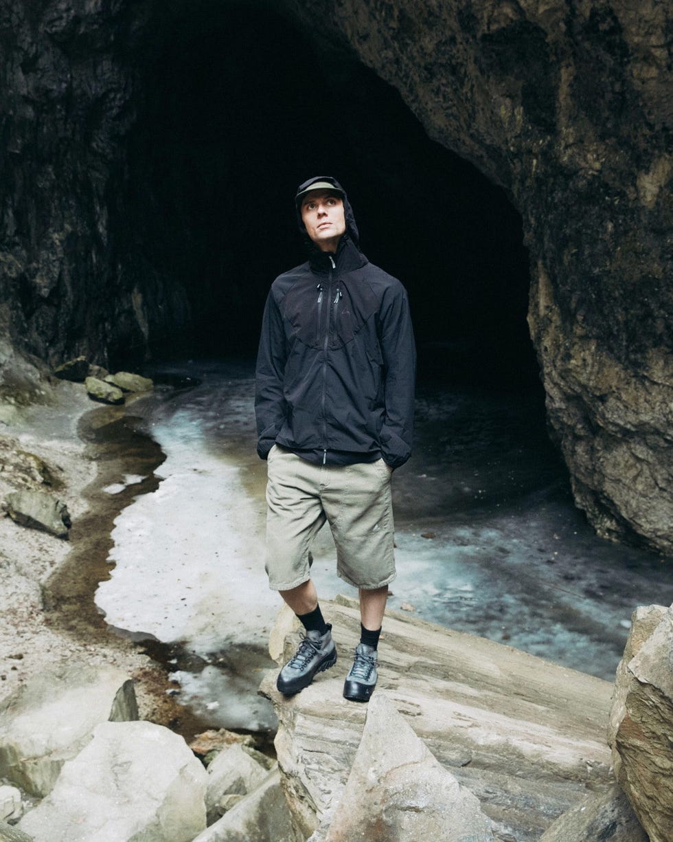 a person standing on rocky terrain near a cave entrance with a water body