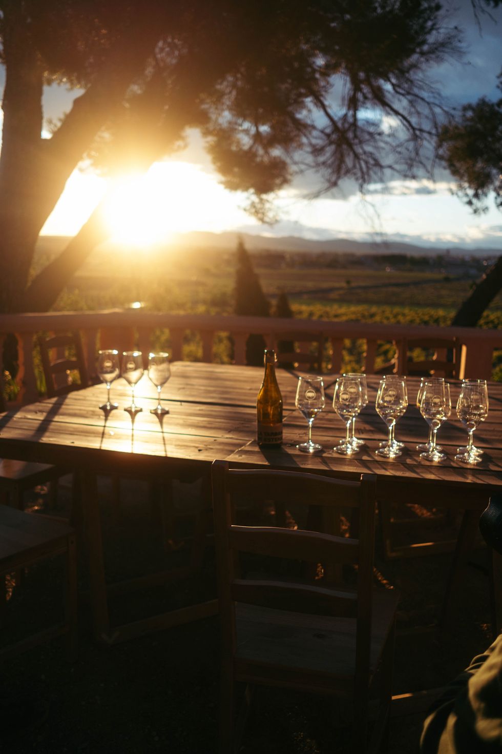 a table with wine glasses and bottles on it with a sunset in the background