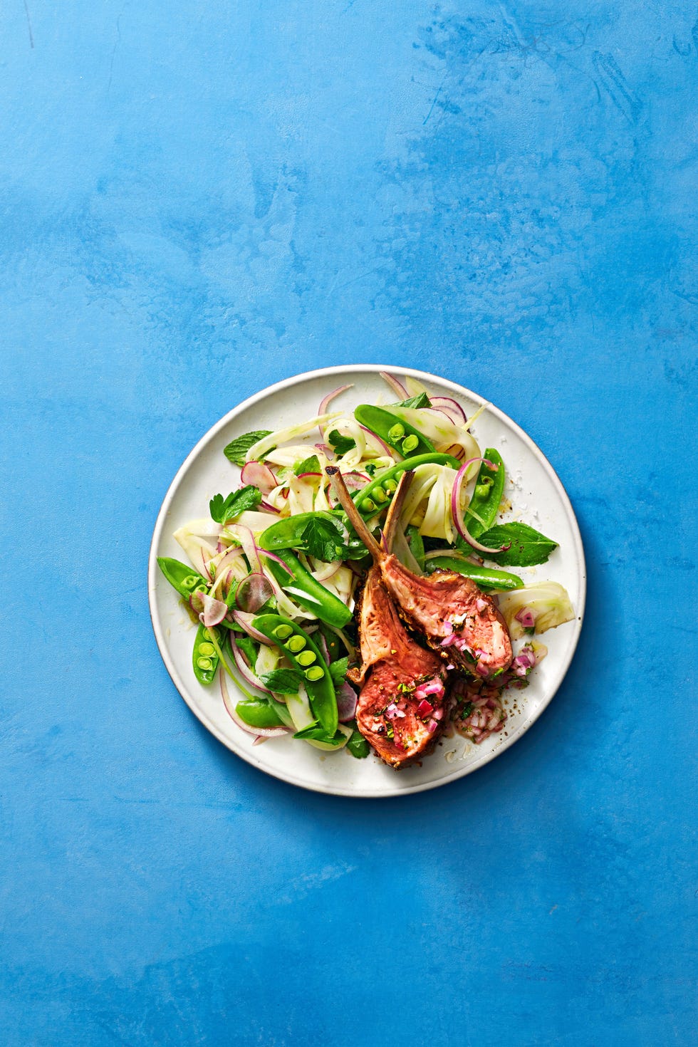 roasted lamb chops with snap pea salad served on a white plate