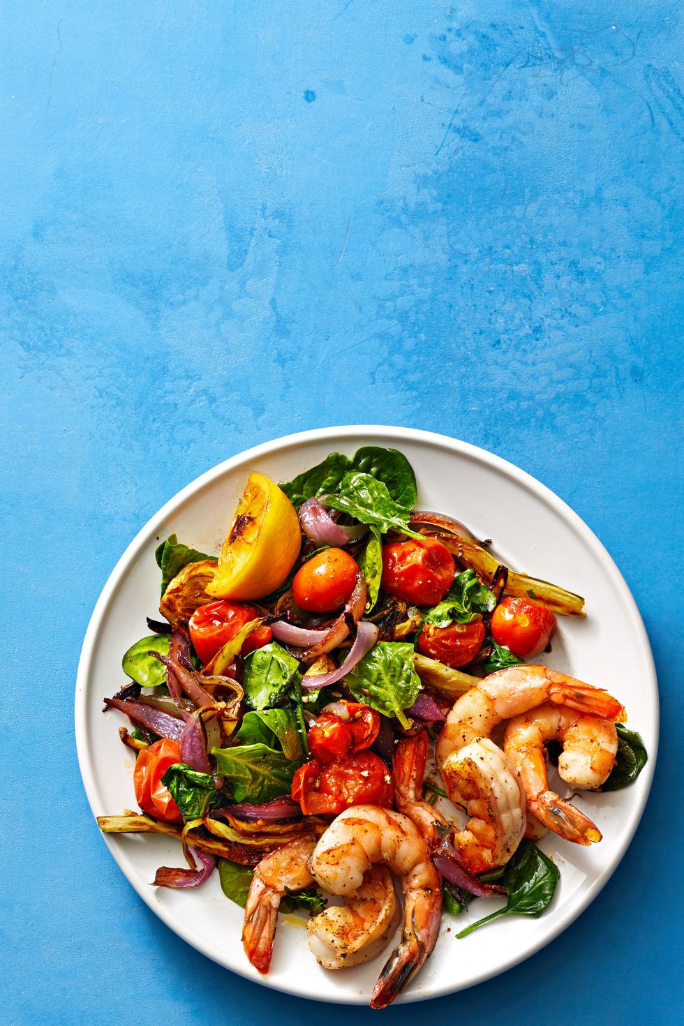 roasted shrimp, tomatoes and spinach on a white plate