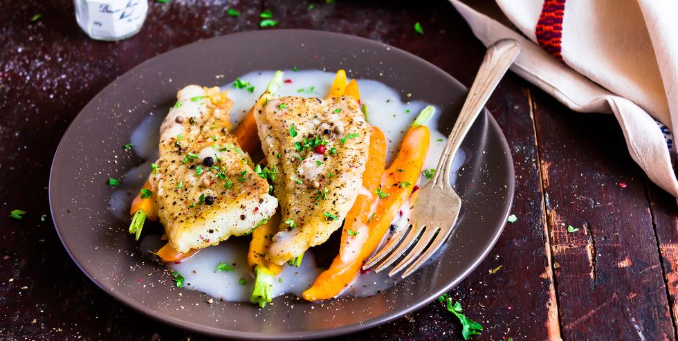 Roasted white fish fillet with cream sauce and baby carrots on a plate, selective focus