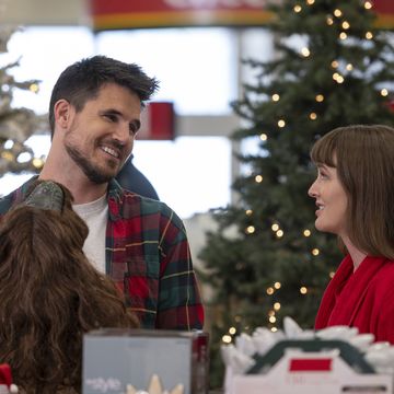 robbie amell and leighton meester star in exmas, a young couple stand in a shop surrounded by christmas decorations and smile at each other