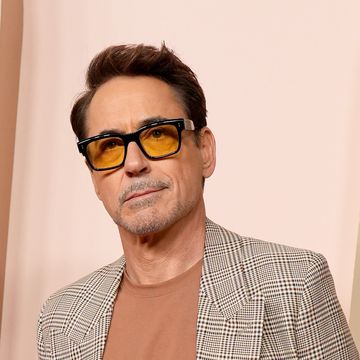 robert downey jr stands in a plaid suit with his hands in his pants pockets, he also wears orange tinted glasses with black frames and a rust orange tshirt