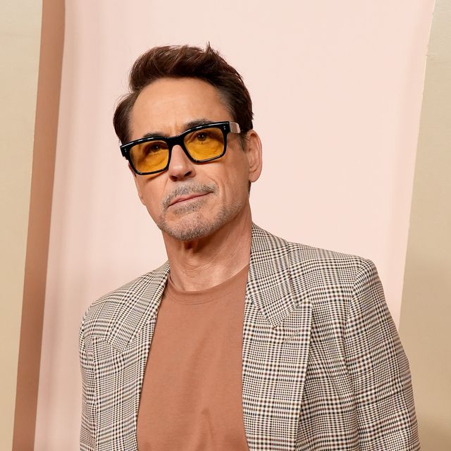 robert downey jr stands in a plaid suit with his hands in his pants pockets, he also wears orange tinted glasses with black frames and a rust orange tshirt