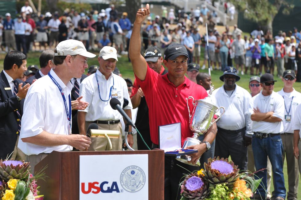 tiger woods holding a trophy and waving to fans