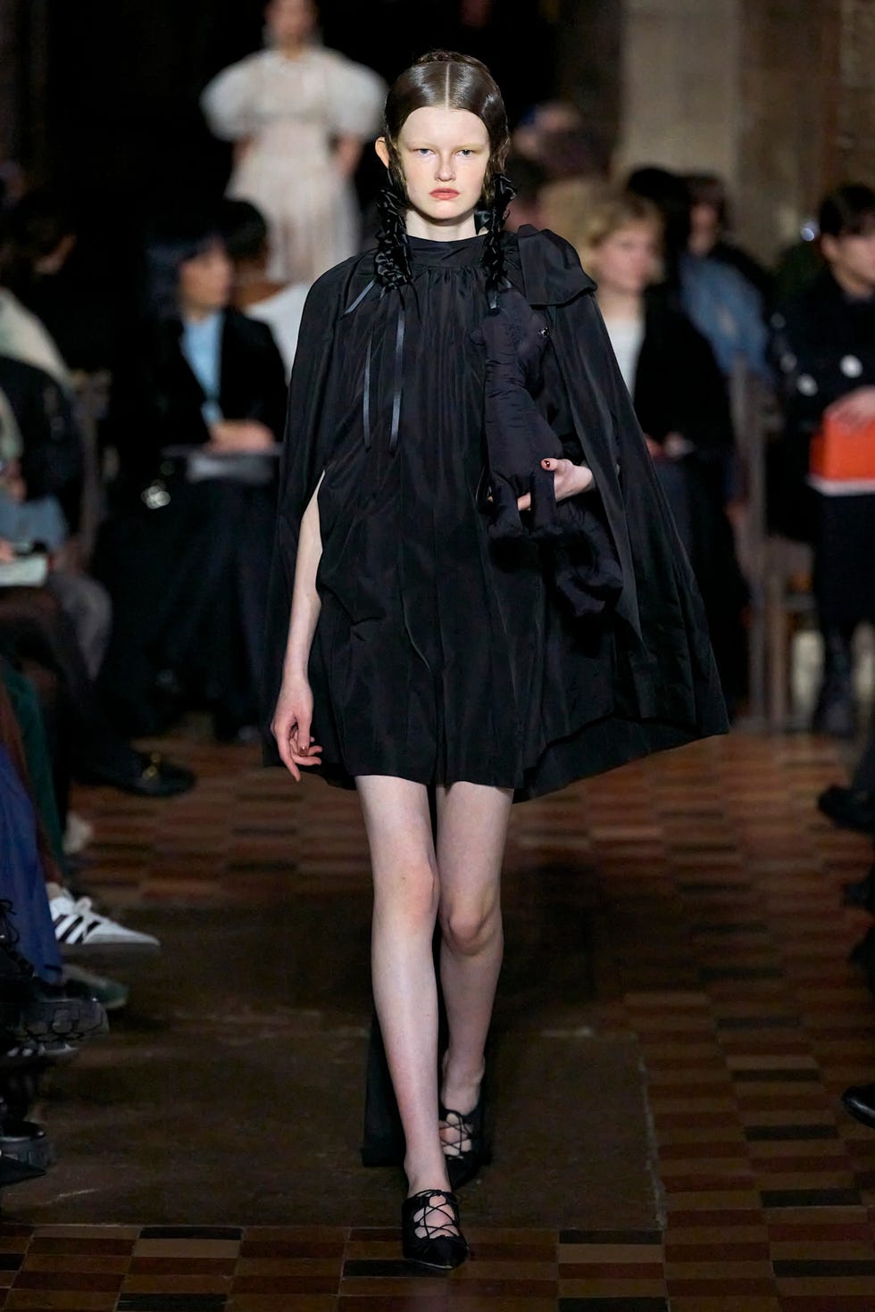 Fashion model on runway wearing a black outfit and holding a toy