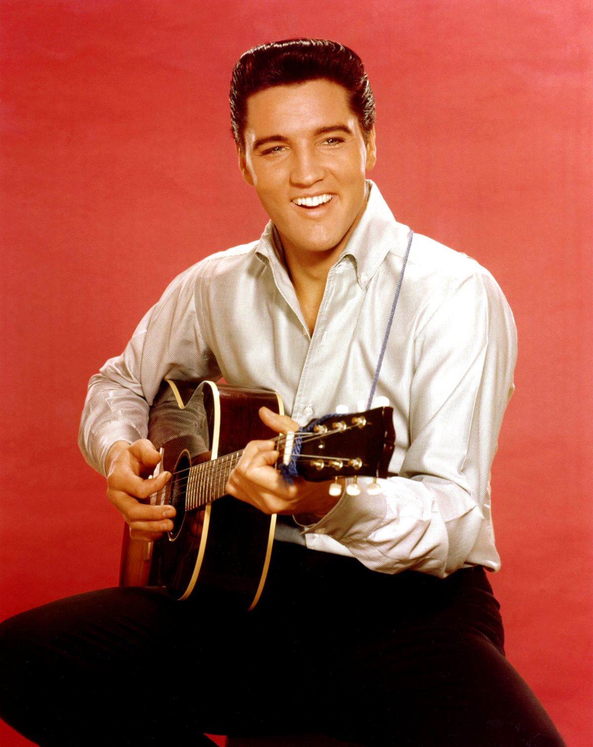 Rock and roll musician Elvis Presley strums an acoustic guitar
