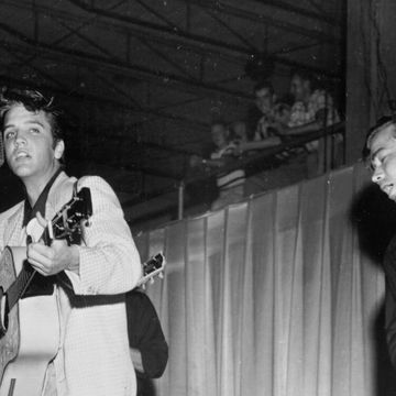 elvis presley playing a guitar and singing into a microphone, an upright bass player plucks his instrument on the right of the frame