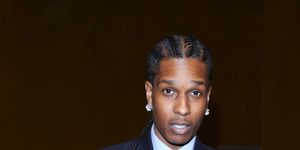 asap rocky looks at the camera as he adjusts his navy pinstripe suit jacket, he also wears a matching tie, white collared shirt, earrings and rings