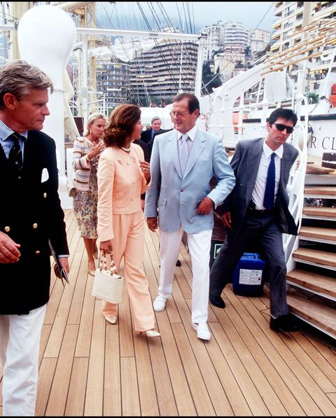 roger moore junto a la reina silvia en el año 2000 con americana azul claro y pantalón blanco