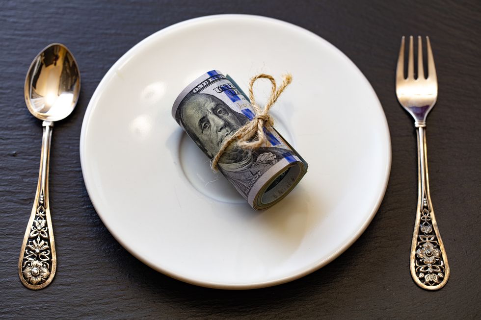roll of 100 dollar banknotes on white plate with small fork and spoon