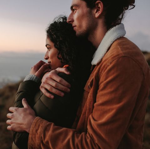romantic young couple standing in mountain together and looking at view young man embracing his girlfriend and looking away