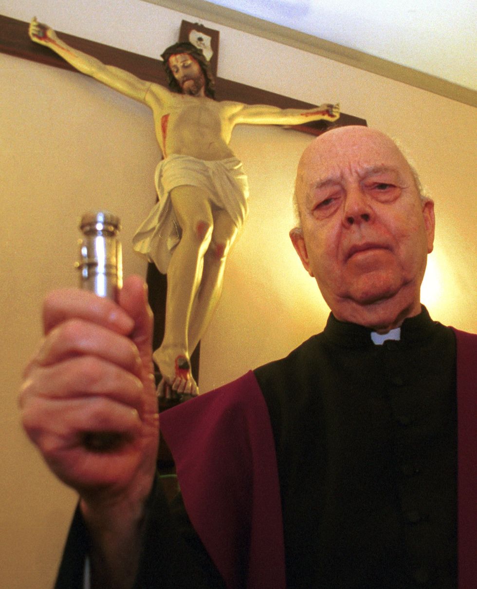 priest holding a vial of holy water in front of a crucifix statue