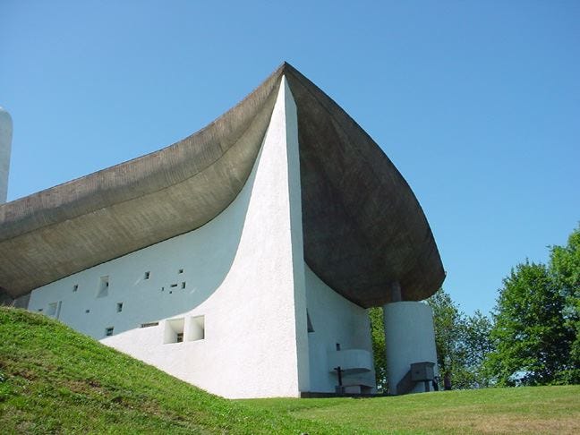 a white building with a triangular roof with notre dame du haut in the background