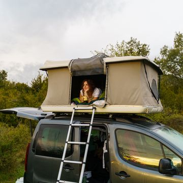 woman looking out of rooftop tent on top of car