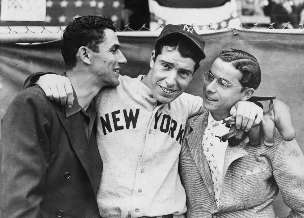 vince dimaggio, joe dimaggio, and dom dimaggio hug and smile, joe wears a new york yankees baseball cap and uniform