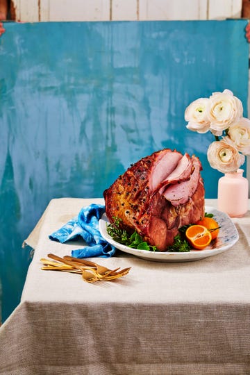 root beer glazed ham on a platter with utensils and a vase with flowers