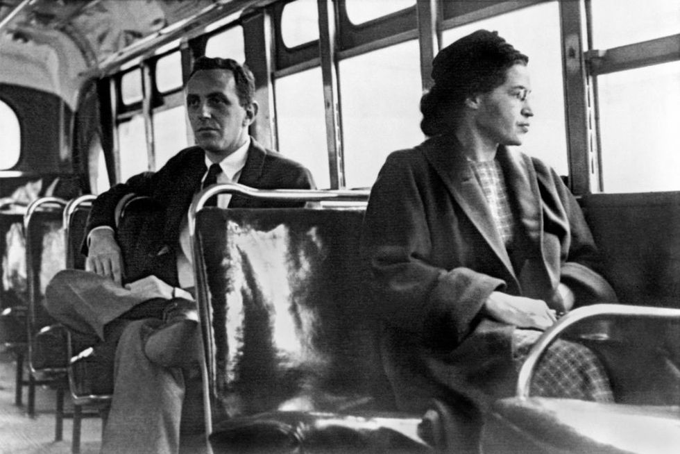 a black and white photograph of rosa park sitting in the seat of a bus, looking out the window, with a man sitting in the seat behind her