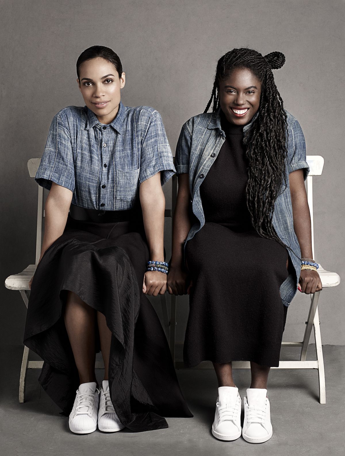 rosario dawson and abrima erwiah sit on a white bench smiling