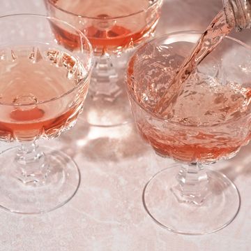 rose sparkling wine or champagne pouring from bottle into crystal glasses on pink marble background. minimal creative composition with copy space.