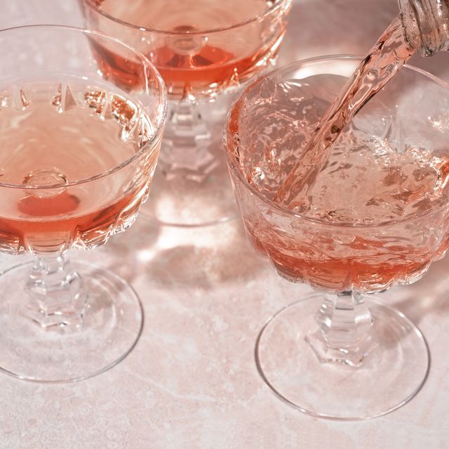 rose sparkling wine or champagne pouring from bottle into crystal glasses on pink marble background. minimal creative composition with copy space.