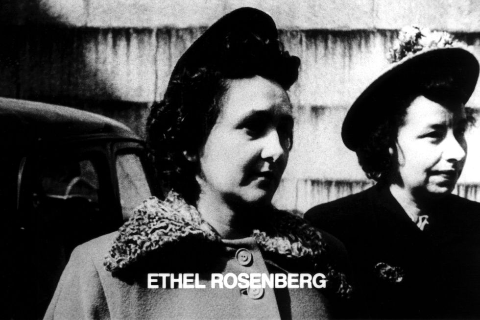 ethel rosenberg looks to the right while standing next to another woman, both wear hats and coats