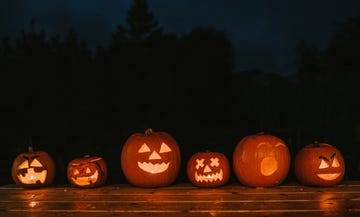 a row of various sized carved hallowe'en pumpkins with different facial expressions glowing in the dark space for copy