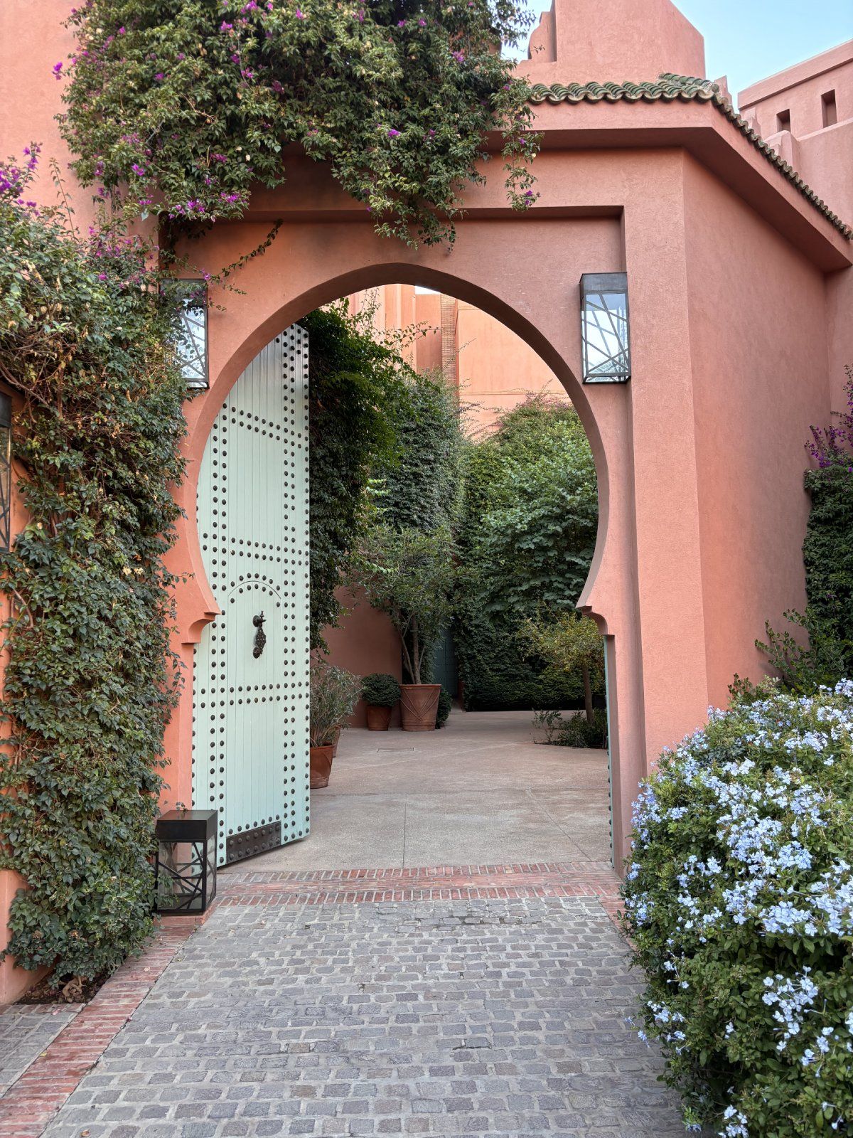 a brick walkway with bushes and a gate