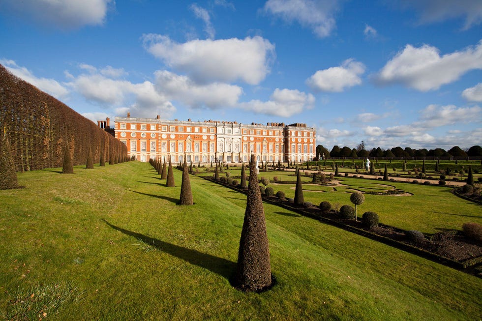 Het Hampton Court Palace dat als een geliefd buitenverblijf voor talloze vorsten diende verrijst boven de formele tuinen in Surrey In Hampton Court is ook de Royal School of Needlework Koninklijke Naaiwerkschool gevestigd waar onder strikte geheimhouding de duizenden kantmotieven voor de bruidsjurk van Kate Middleton werden opgebracht De bruidsjurk van Meghan Markle werd ontworpen door de Britse modedesigner Clare Waight Keller