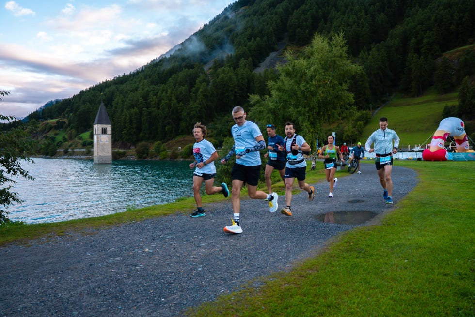 a group of runners participating in an outdoor event near a lake with a bell tower in the background