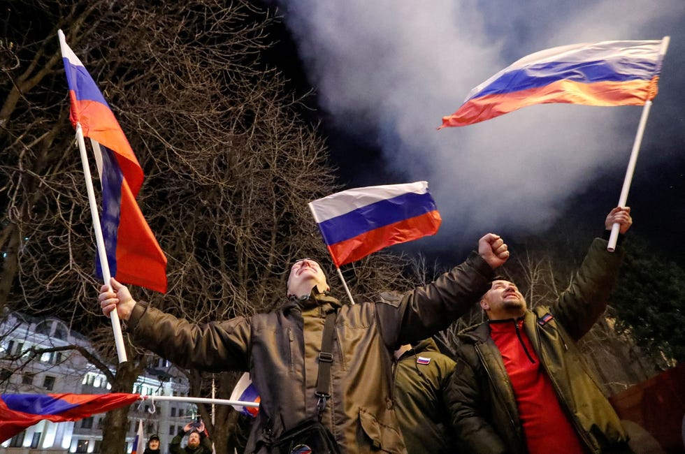 Pro-Russian activists react on a street in Donetsk ProRussische activisten vieren feest in de straten van het door separatisten gecontroleerde Donetsk nadat Poetin een decreet had ondertekend waarin twee door Rusland gesteunde afgescheiden regios in OostOekrane als onafhankelijke entiteiten worden erkend Achter hen explodeert vuurwerk in de lucht