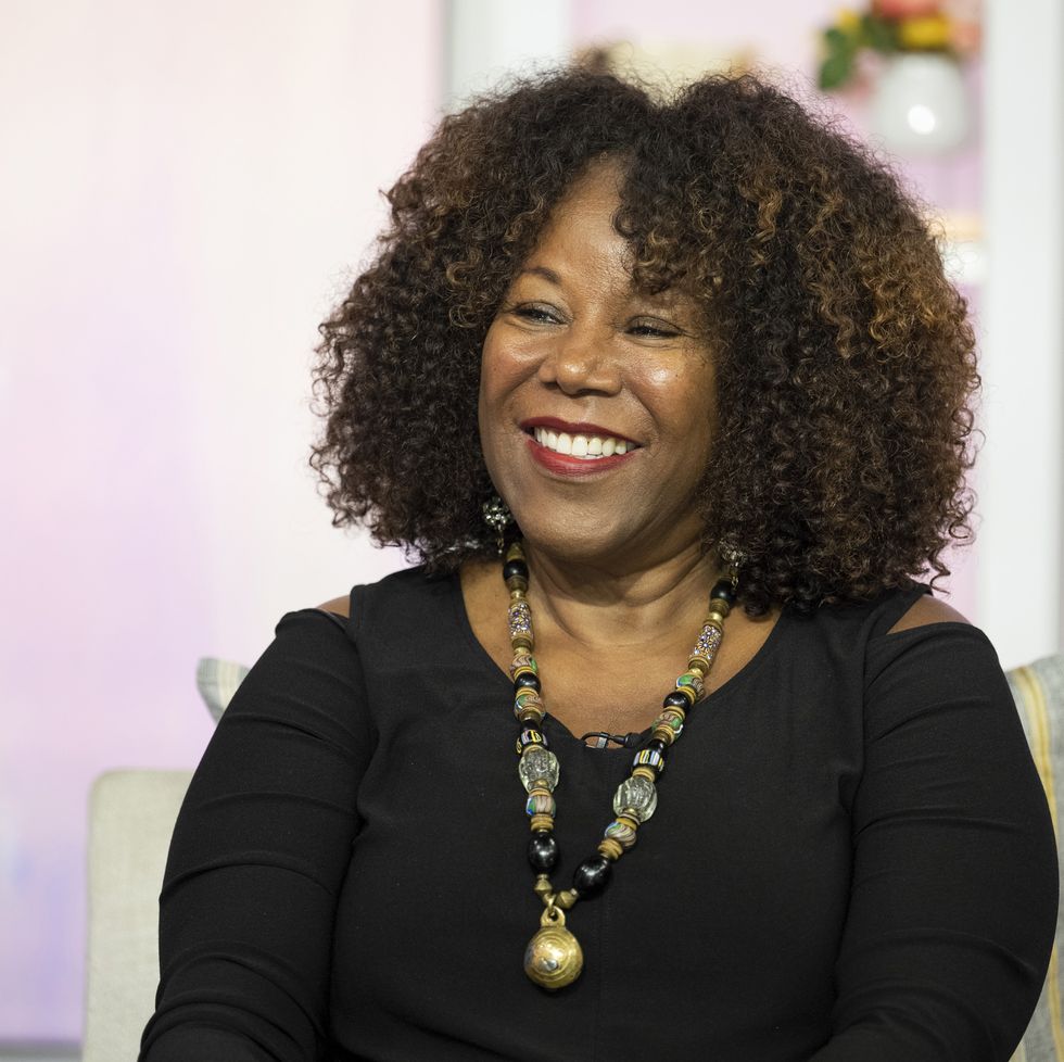 ruby bridges smiles and looks left, she wears a dark long sleeve shirt with a large beaded necklace, she sits in a chair with a pillow behind her