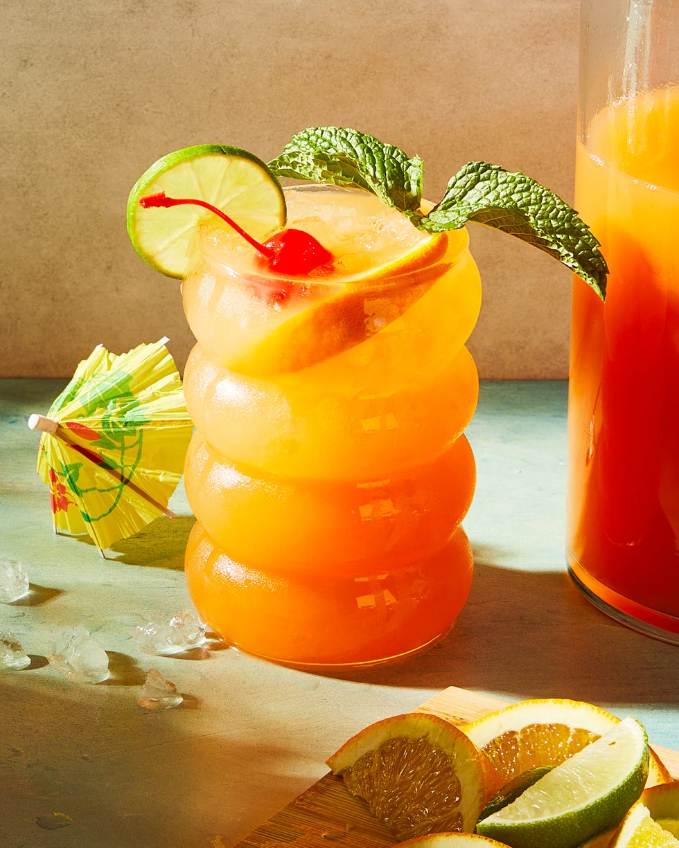 rum punch cocktail in a glass with mint, an orange slice, a lime wheel, and a maraschino cherry
