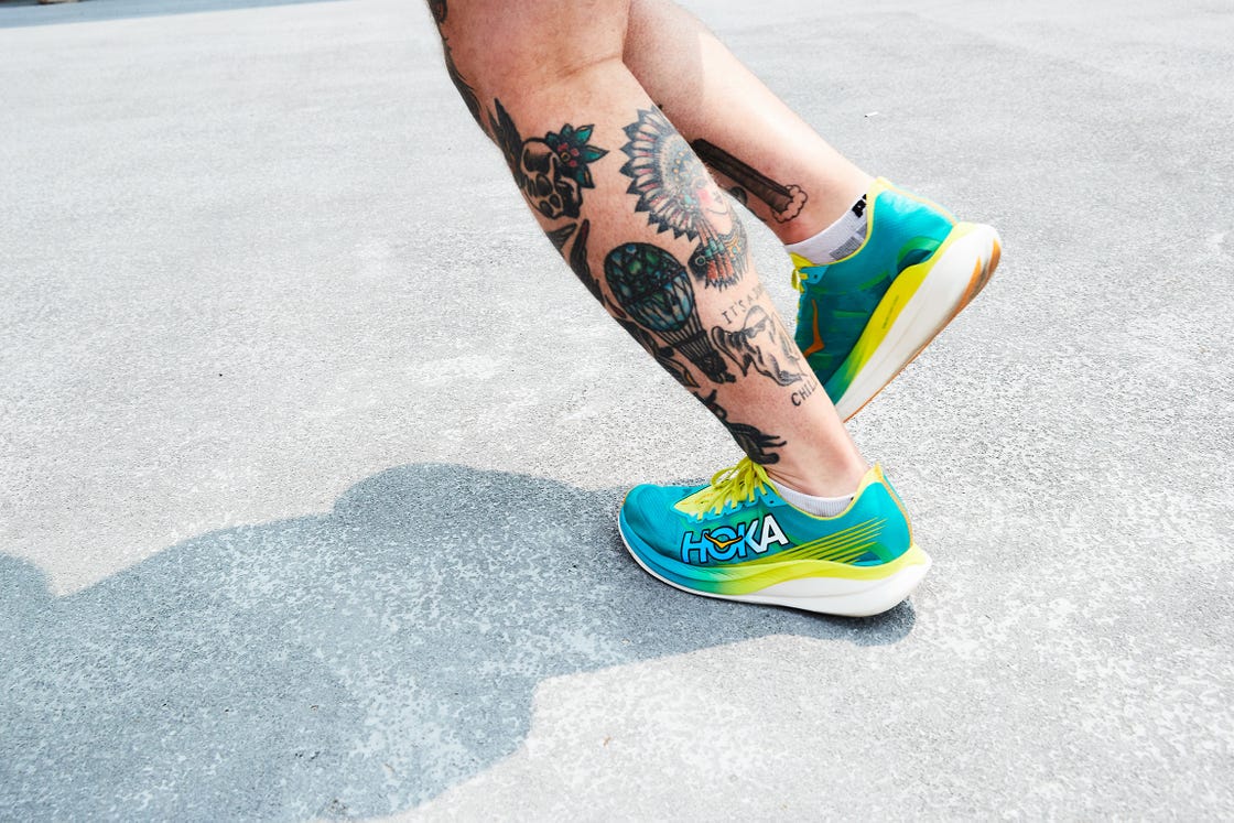 person with tattooed calves jogging in hoka running shoes