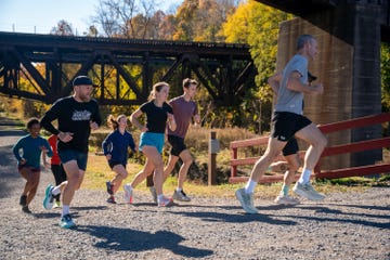 a group of people running on a gravel path near a bridge