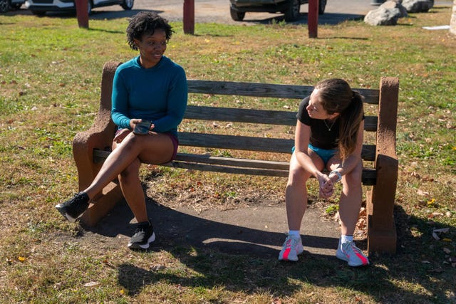 two individuals seated on a park bench engaged in separate activities