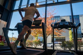 person jogging on a treadmill inside a gym with a view of autumn trees through large windows