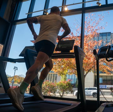 Person jogging on a treadmill inside a gym with a view of autumn trees through large windows person jogging on a treadmill inside a gym with a view of autumn trees through large windows