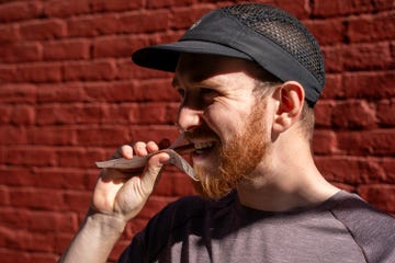 person holding a device near their mouth against a red brick wall