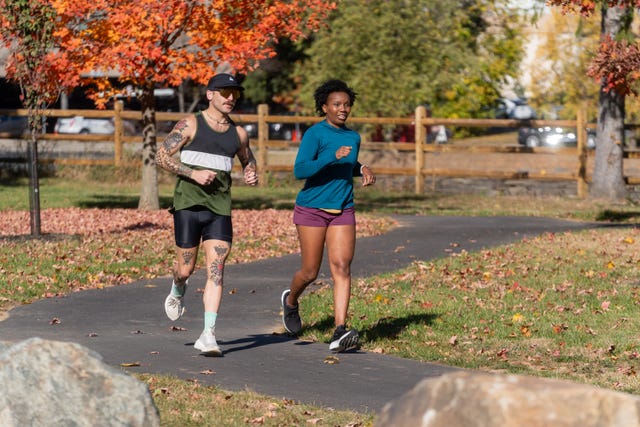 two individuals jogging on a pathway surrounded by autumn foliage