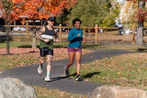 two individuals jogging on a pathway surrounded by autumn foliage