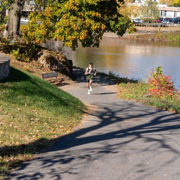 A person jogging along a path by a body of water surrounded by trees a person jogging along a path by a body of water surrounded by trees