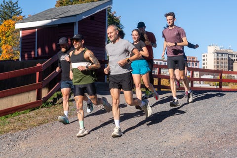 group of runners on a gravel path with a red wooden railing and a building in the background