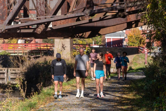 group of people walking and running along a path under a rusty bridge