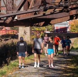 Group of people walking and running along a path under a rusty bridge group of people walking and running along a path under a rusty bridge