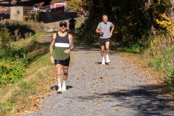 two individuals jogging on a gravel path surrounded by trees and autumn foliage