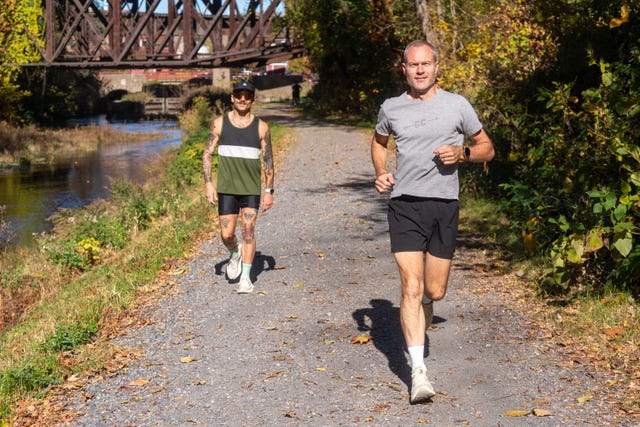 two individuals jogging along a gravel path by a waterway