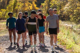 group of individuals walking along a gravel path in a wooded area during autumn