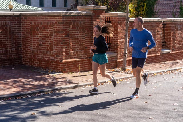 two individuals jogging along a brick wall on a sunny day