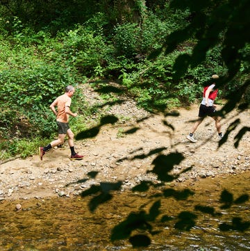 best trail running shoes two runners on a dirt path next to a stream in a forested area